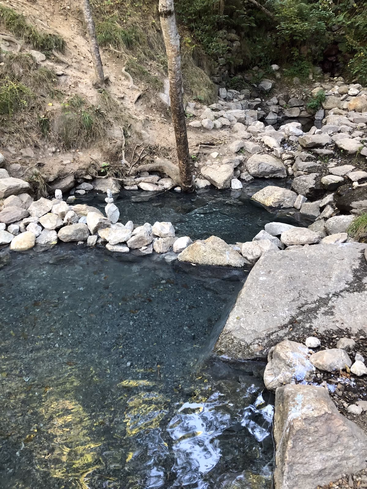 Rock-lined natural hot spring pool at Sources Chaudes de Merens-les-Vals with clear water and surrounding trees in southern France.