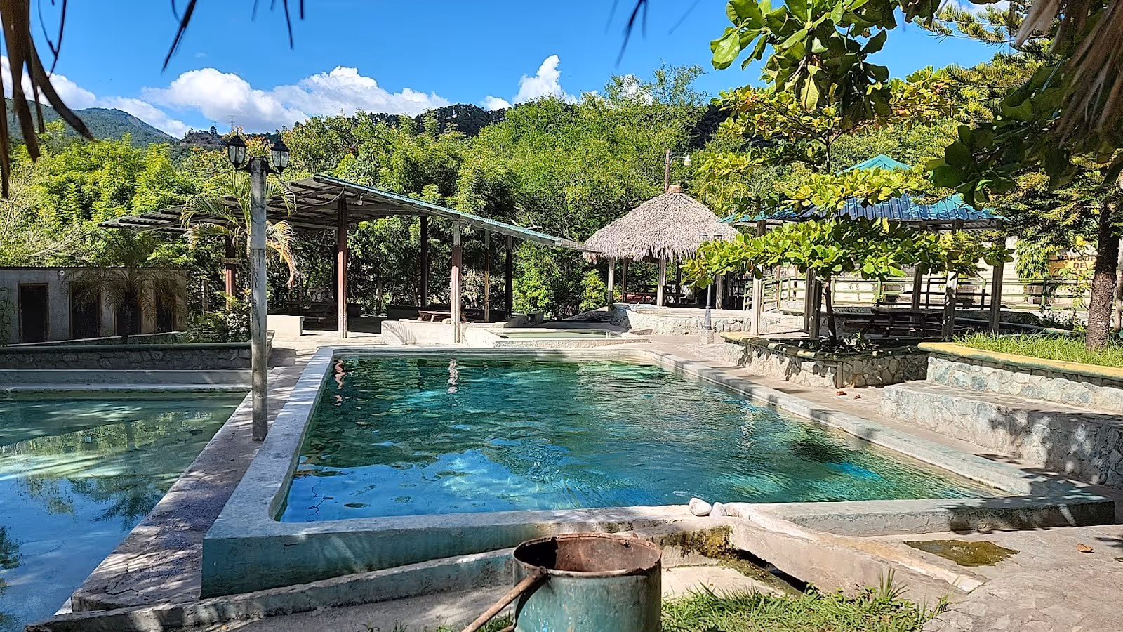 Outdoor hot spring pools at Banos Termales El Brasilar with shaded sitting areas and lush green trees near Camotan Guatemala.