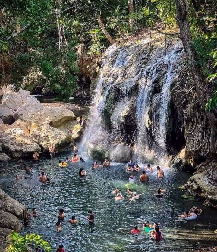 People soaking in the outdoor natural hot spring pool with a cascading waterfall surrounded by dense greenery at Finca El Paraiso near El E.