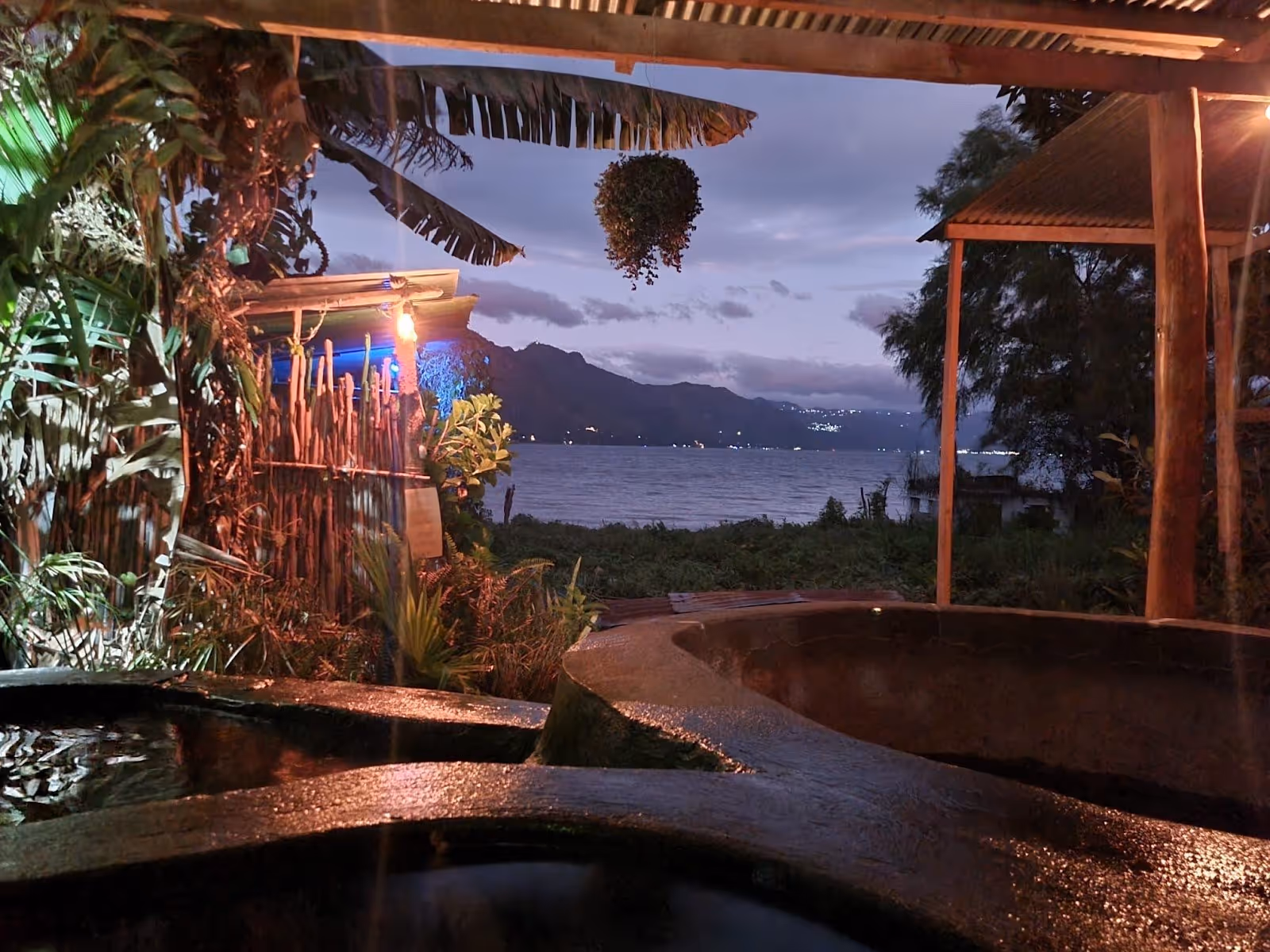 Nighttime view of Los Termales hot spring pools lit with colorful lights, overlooking Lake Atitlan and mountains in Guatemala.