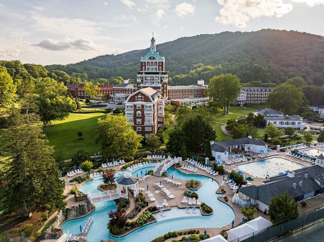 Red brick tower and resort with outdoor pools against the backdrop of allegheny mountains at omni homestead resort in virginia