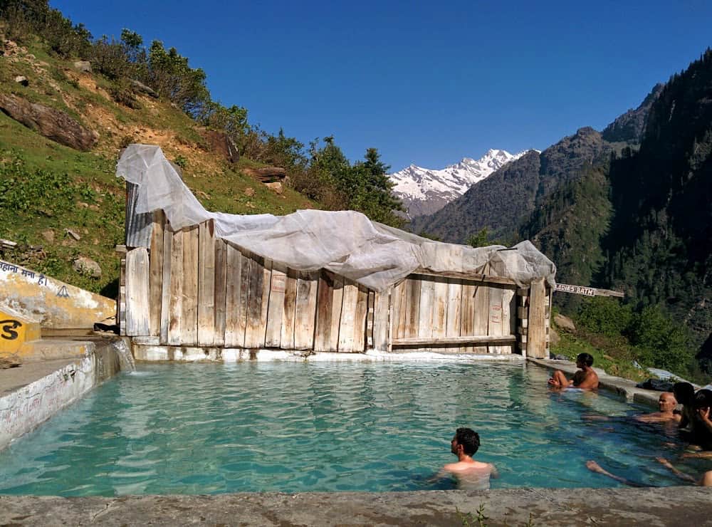 man soaking at a geothermal hot spring pool in high-altitude himalayan meadow at kheer ganga hot spring in india