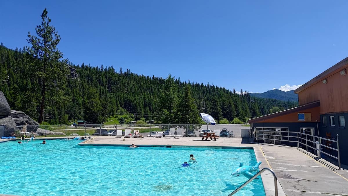 People soaking in an outdoor hot spring pool with forested valley views in lolo hot springs montana