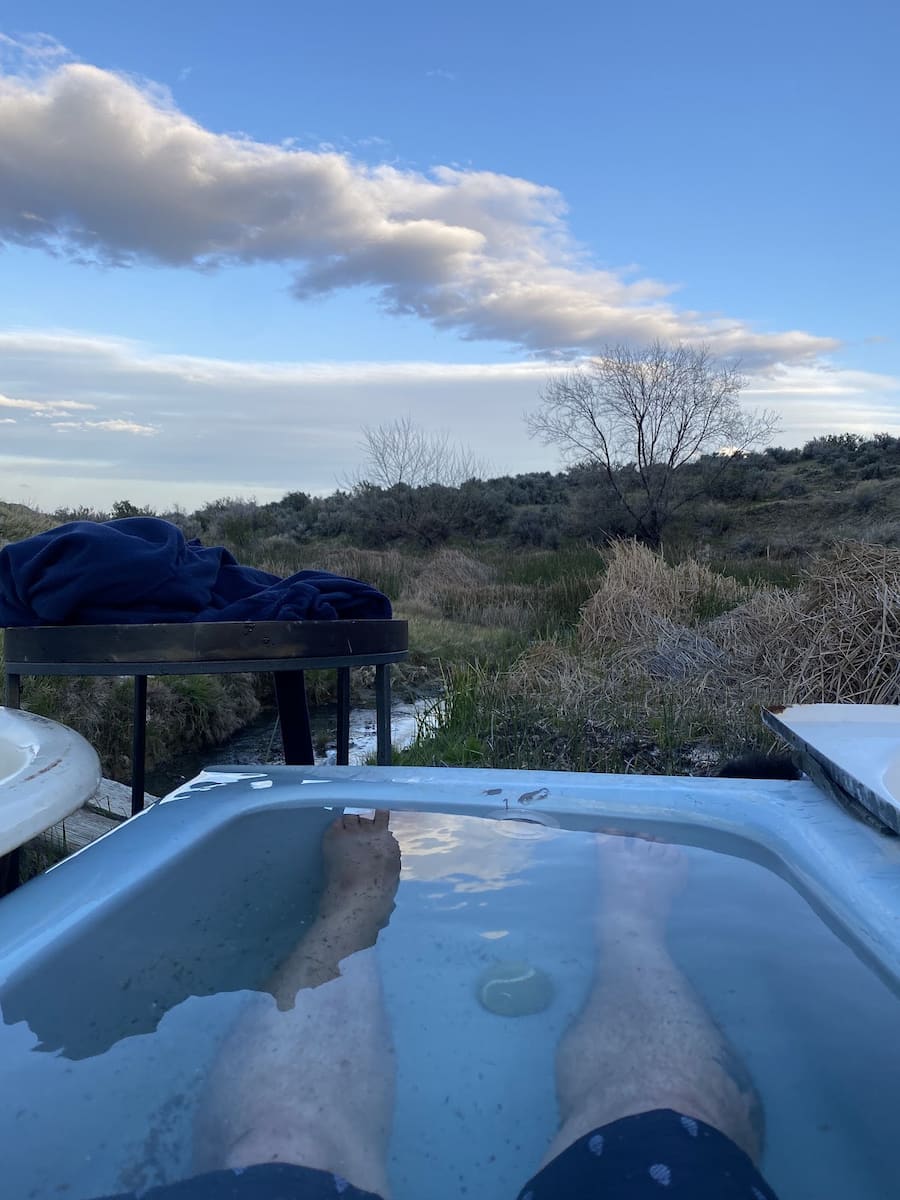person soaking in outdoor hot spring tub with semi-desert views at dyke hot springs nevada
