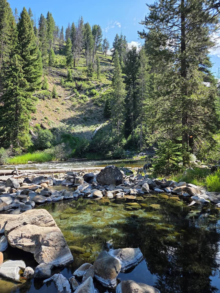 natural hot spring pool on a river bank in a forest setting at bear valley hot spring idaho