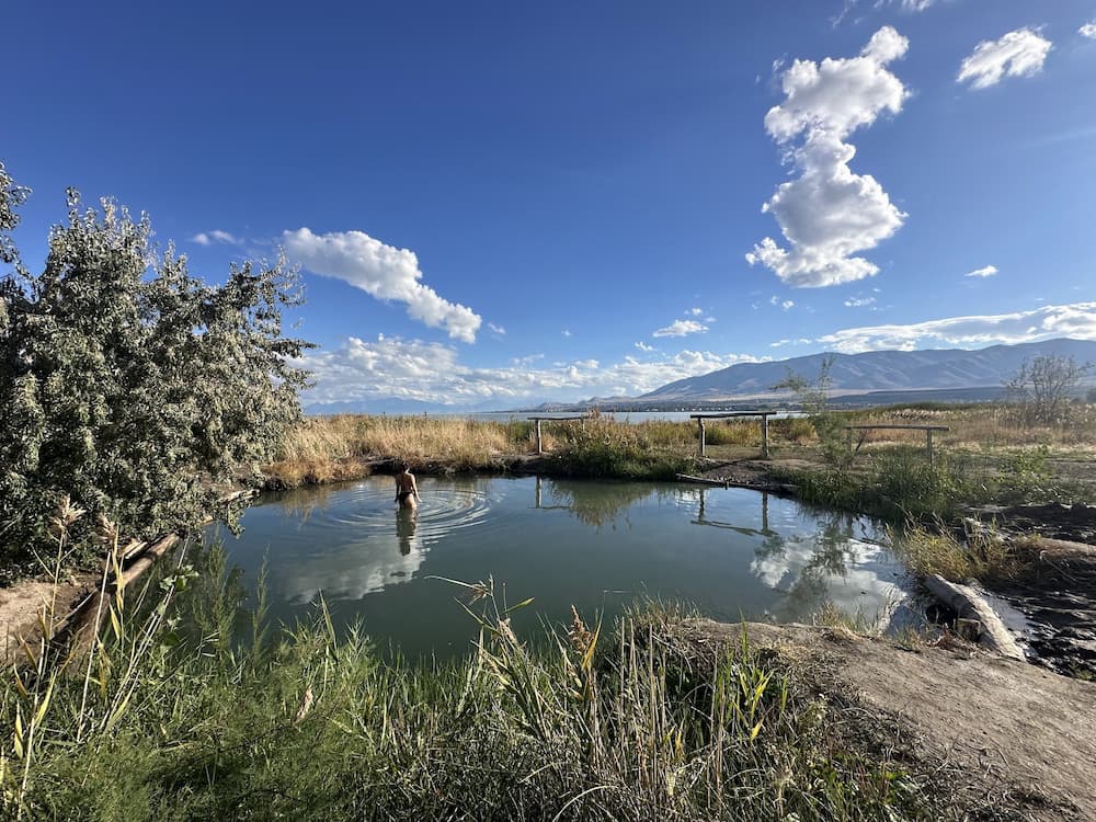 Person soaking at a natural hot spring pool with mountains in the background at saratoga hot springs utah