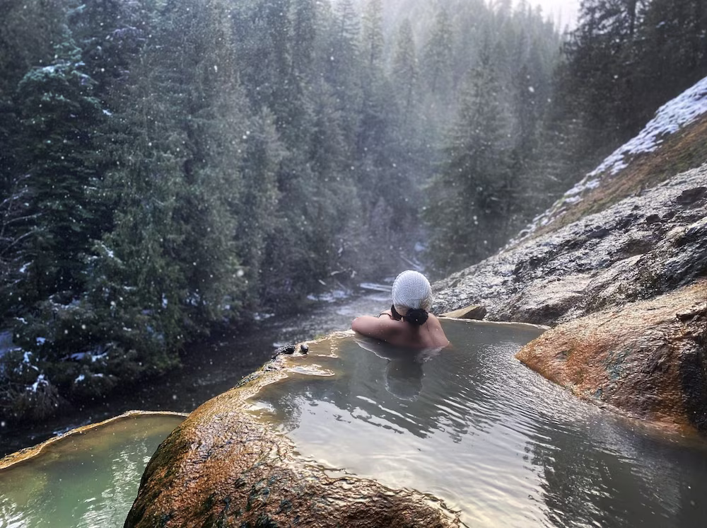 person soaking in a cliffside hot spring pool with forest views in winter at umpqua hot springs oregon