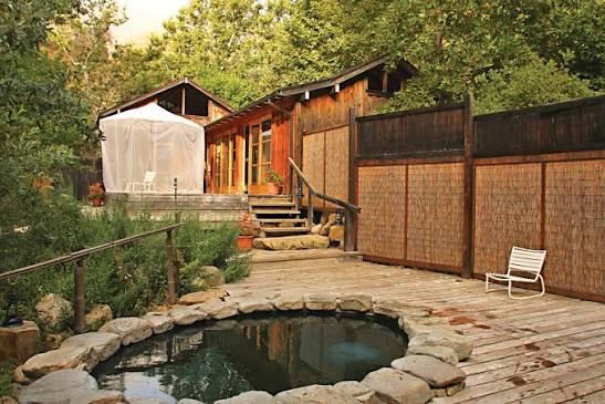 Outdoor private hot spring tub with resort building and lush vegetation in the background at tassajara hot springs in california