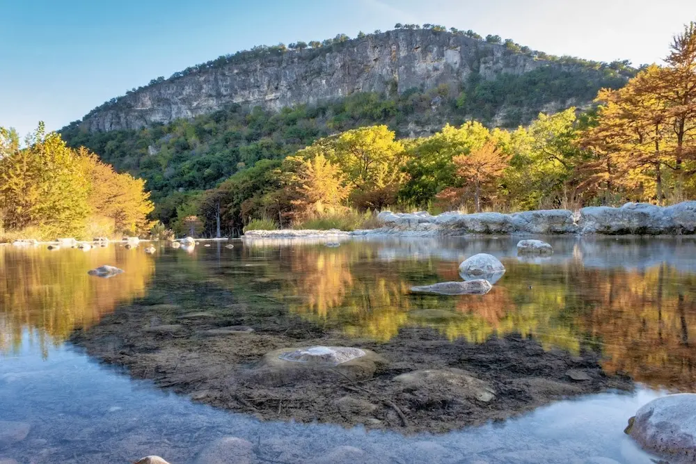 Outdoor natural springs pool with mirror reflection of autumn forest and hills in the background at garner state park in texas