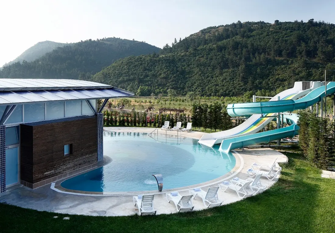 Outdoor hot spring pool with waterslides, resort and mountain views in the background at obam thermal resort in turkey