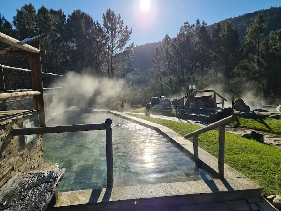 Outdoor steaming hot spring pools in a natural setting and mountains in the background at termas de prexigueiro in spain