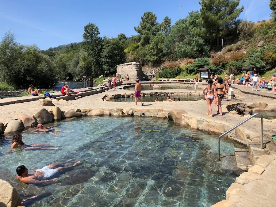 People soaking in clear water outdoor hot spring pools in termas do muino da veiga in spain