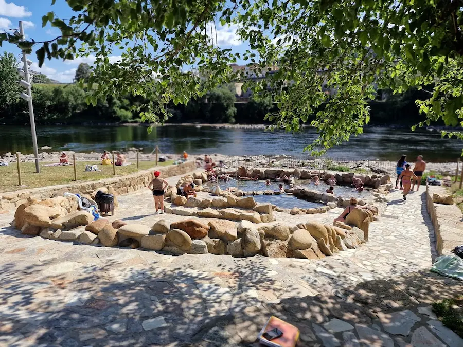 People soaking at outdoor rock lined hot spring pools next to a river at pozas da chavasqueira in spain