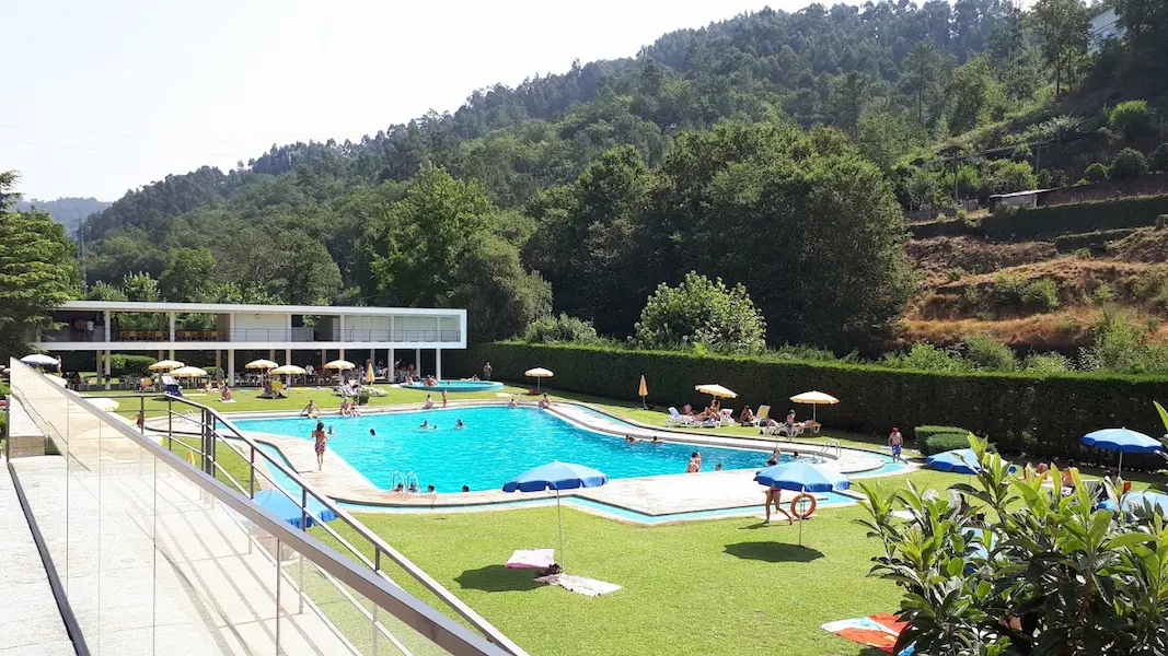 Thermal spa complex with outdoor pool and mountains in the background at termas de caldelas in portugal