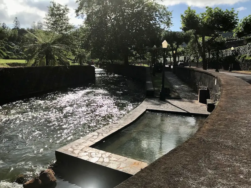 Developed outdoor hot spring pool above a river shaded by trees at poca da tia silvina in portugal