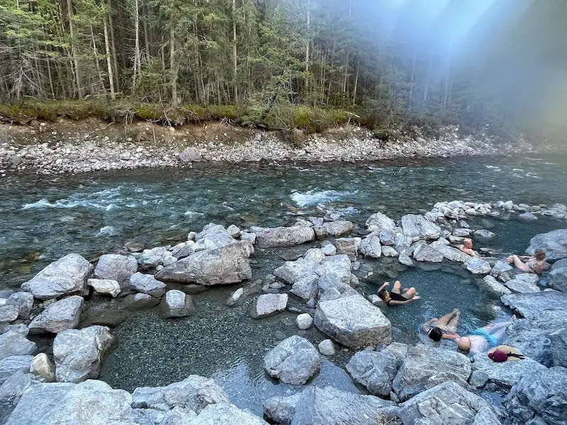 People soaking in outdoor natural hot spring pools beside the lussier river at lussier hot springs in canada