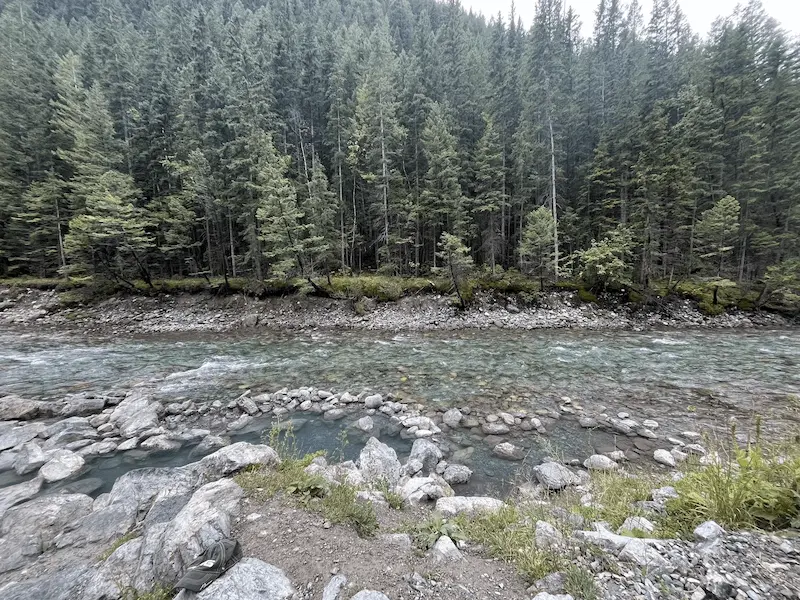 Rock lined natural hot spring pools beside the lussier river and with forest in the background at lussier hot springs in canada