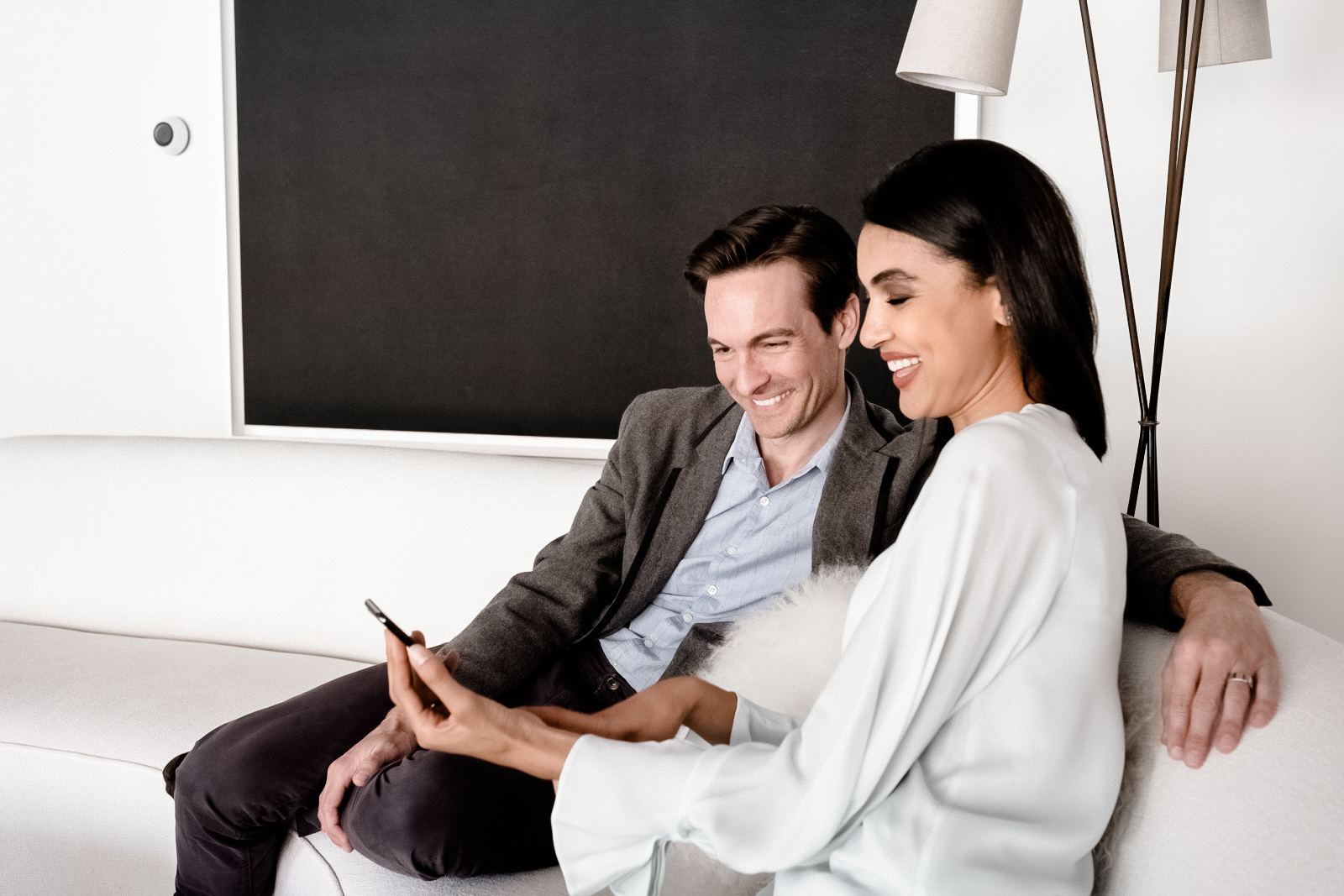 Couple on a sofa, one holding a phone, blackout shade behind