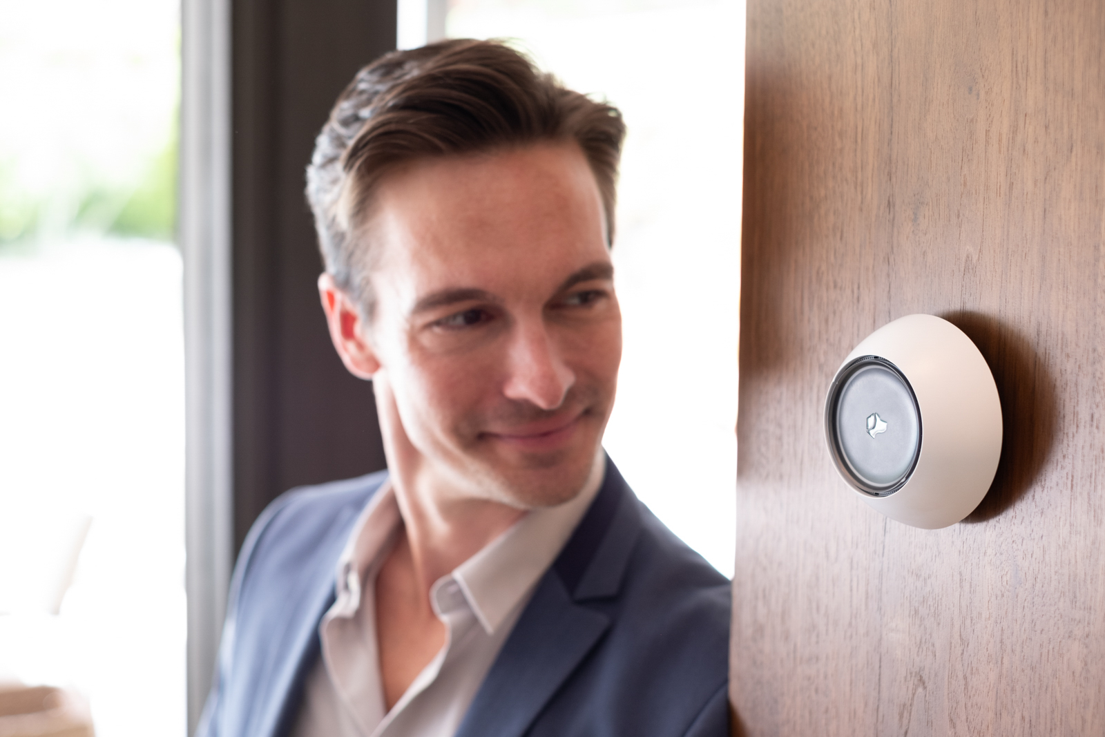Man in a blazer beside a Josh Micro on a wood entryway wall