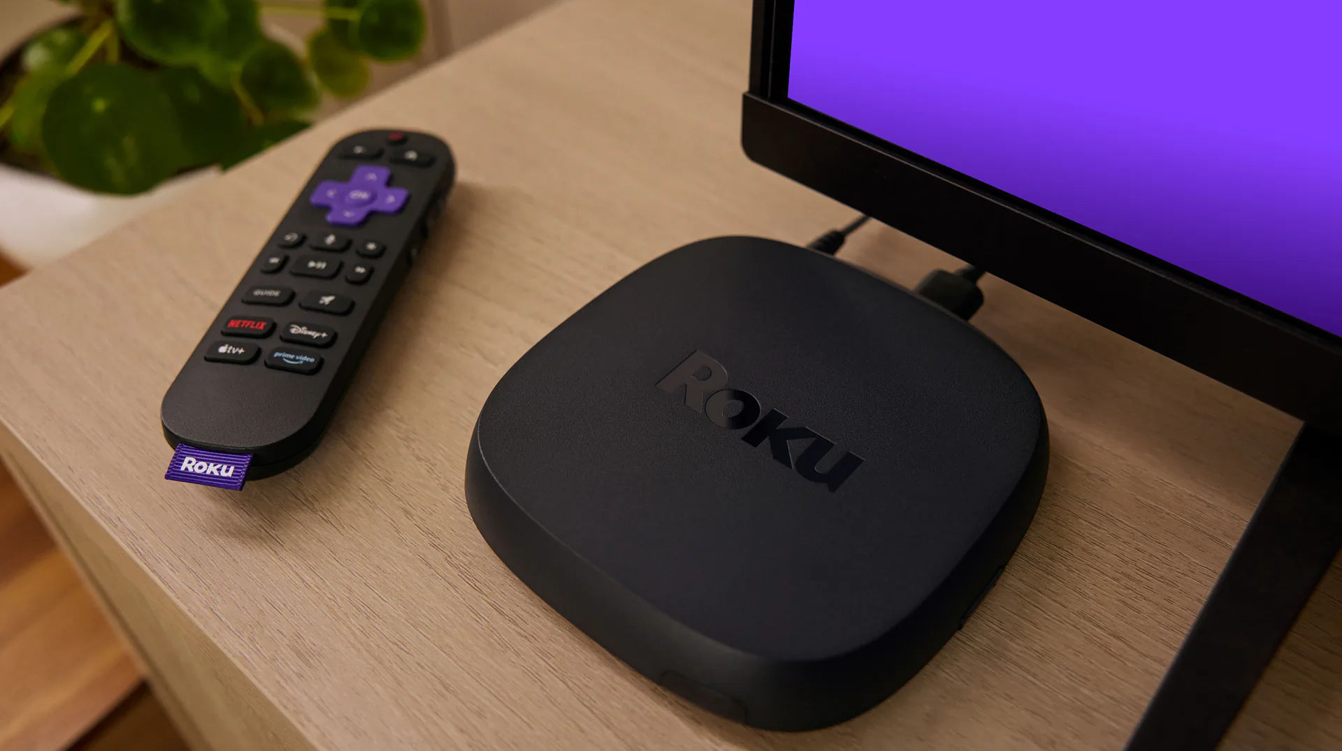 Roku Ultra streaming player and remote on a desk beside a television