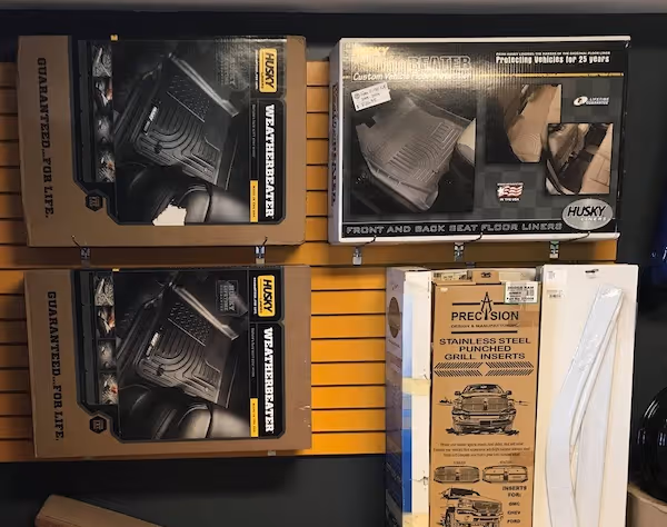 Display of Husky WeatherBeater floor liners and Precision stainless steel punched grill inserts in their packaging on a store wall.