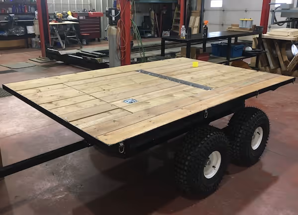 Custom flatbed trailer with wooden plank surface and four off-road tires in a workshop.