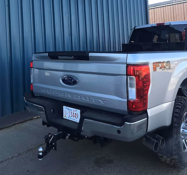 Rear view of a silver Ford Super Duty FX4 Off Road pickup truck parked beside a blue metal wall.