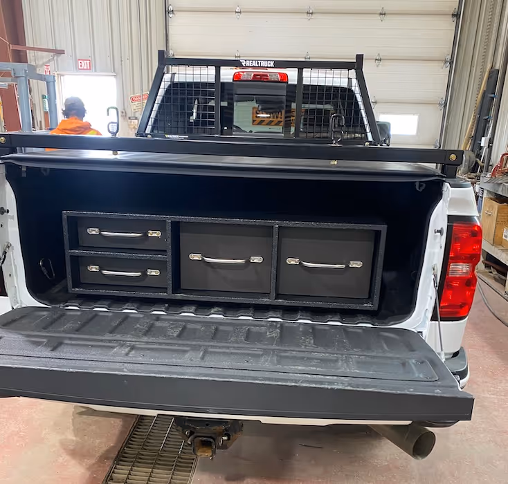 White pickup truck with an open tailgate showing a custom black storage drawer system installed inside the truck bed.