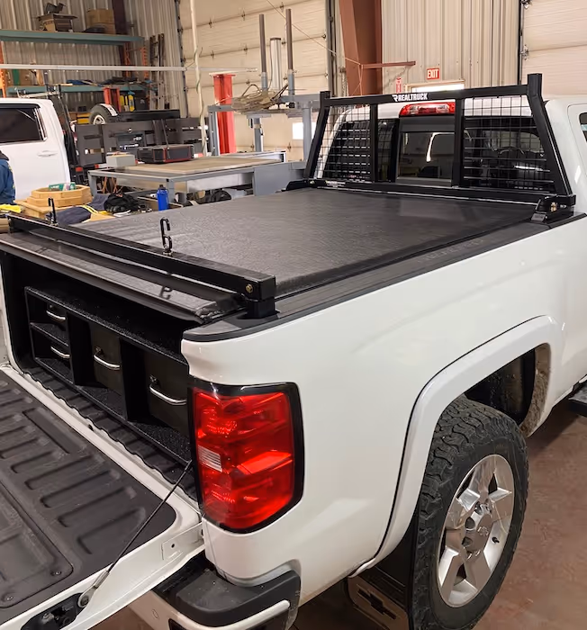 White pickup truck in a garage with a closed black tonneau cover and a black headache rack installed.