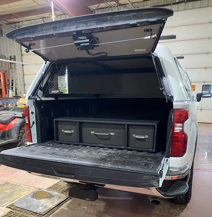White pickup truck with open bed canopy showing installed black storage drawers inside the truck bed.