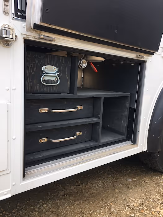 Open compartment of a vehicle showing custom black wooden storage drawers and shelves.