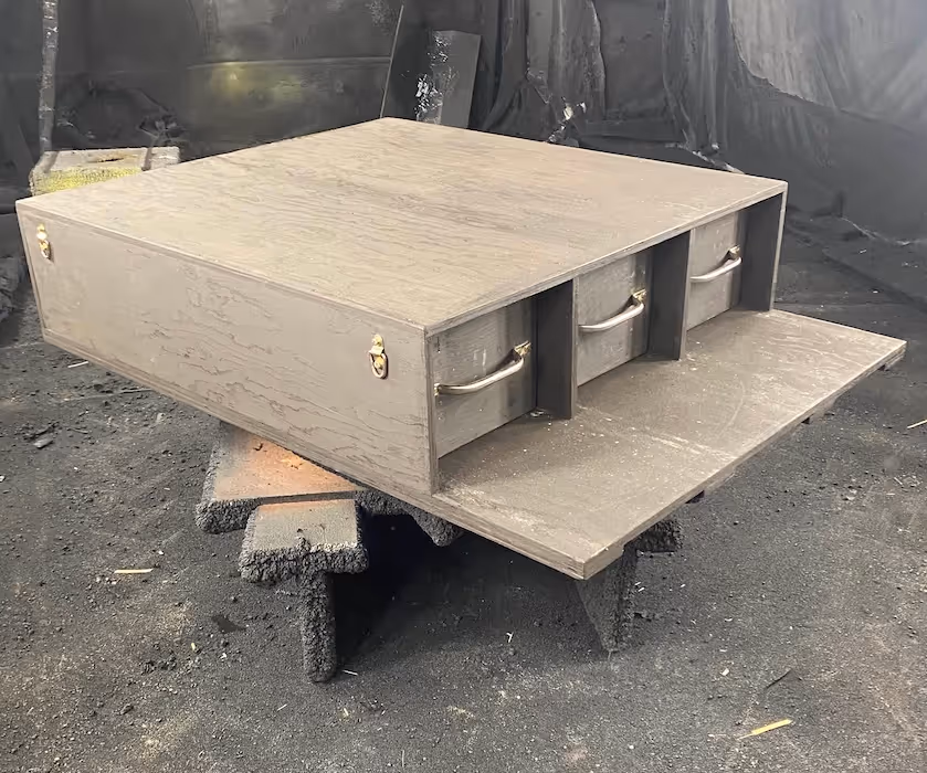 Wooden box with three metal drawers, sitting on two makeshift supports in a dimly lit workshop.