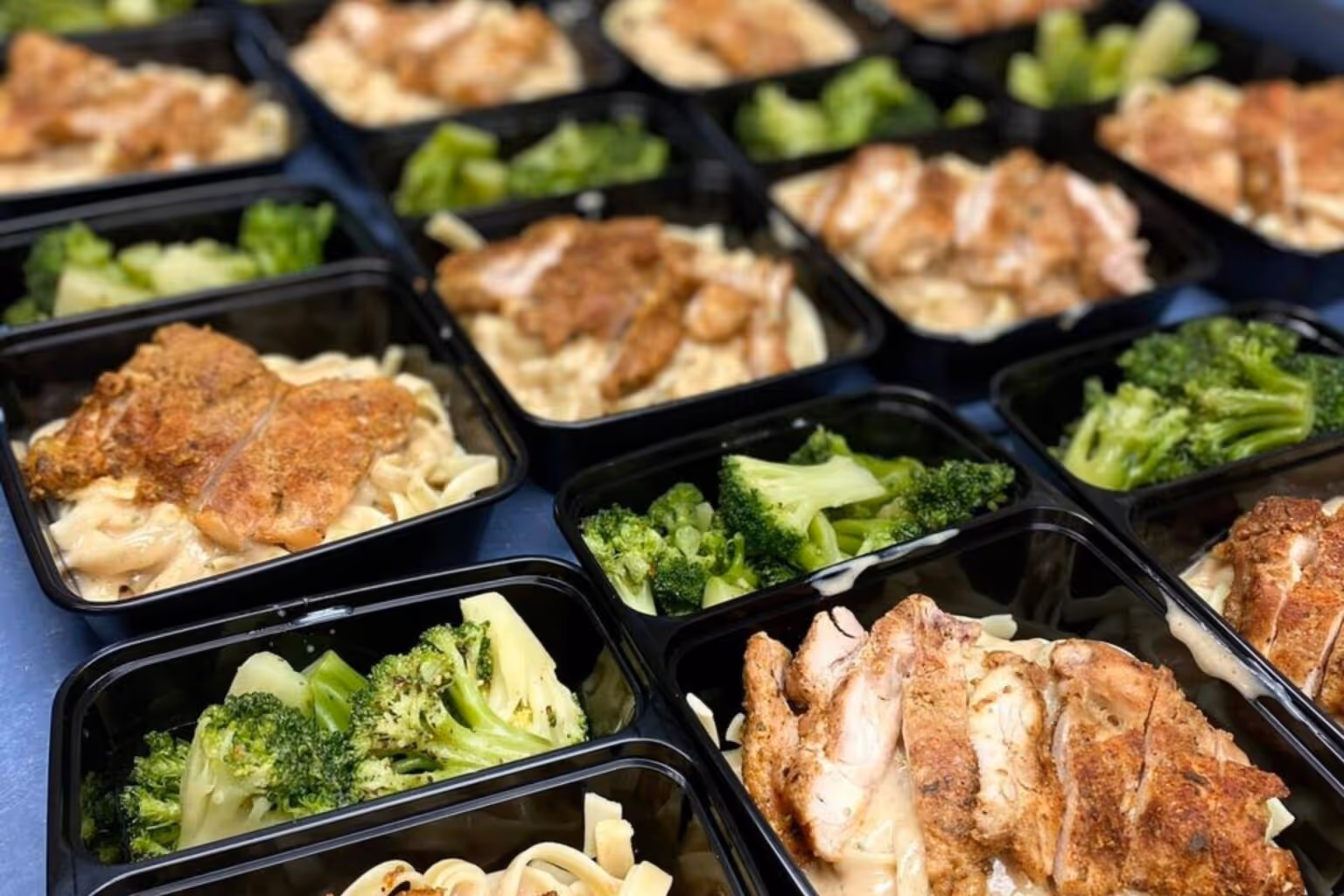 A photo of grilled chicken over alfredo pasta with a side of broccoli, packed in containers for distribution at the Master's Kitchen.