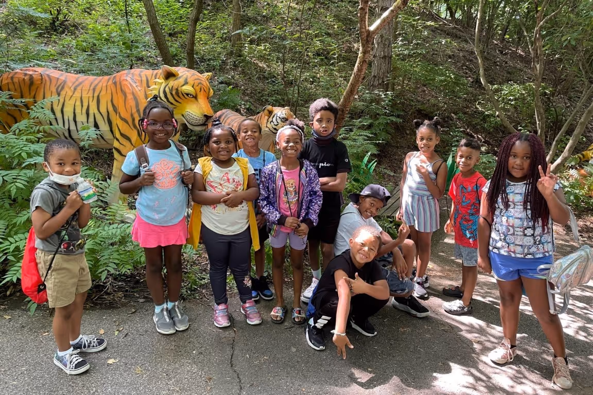 A group of students from the DiSYPles summer camp program pose for a photo in front of a tiger statue at the zoo.