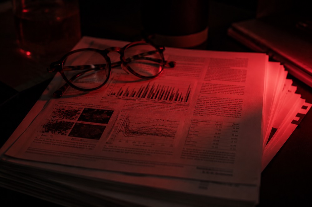 A stack of printed clinical journal pages under red light with reading glasses on top