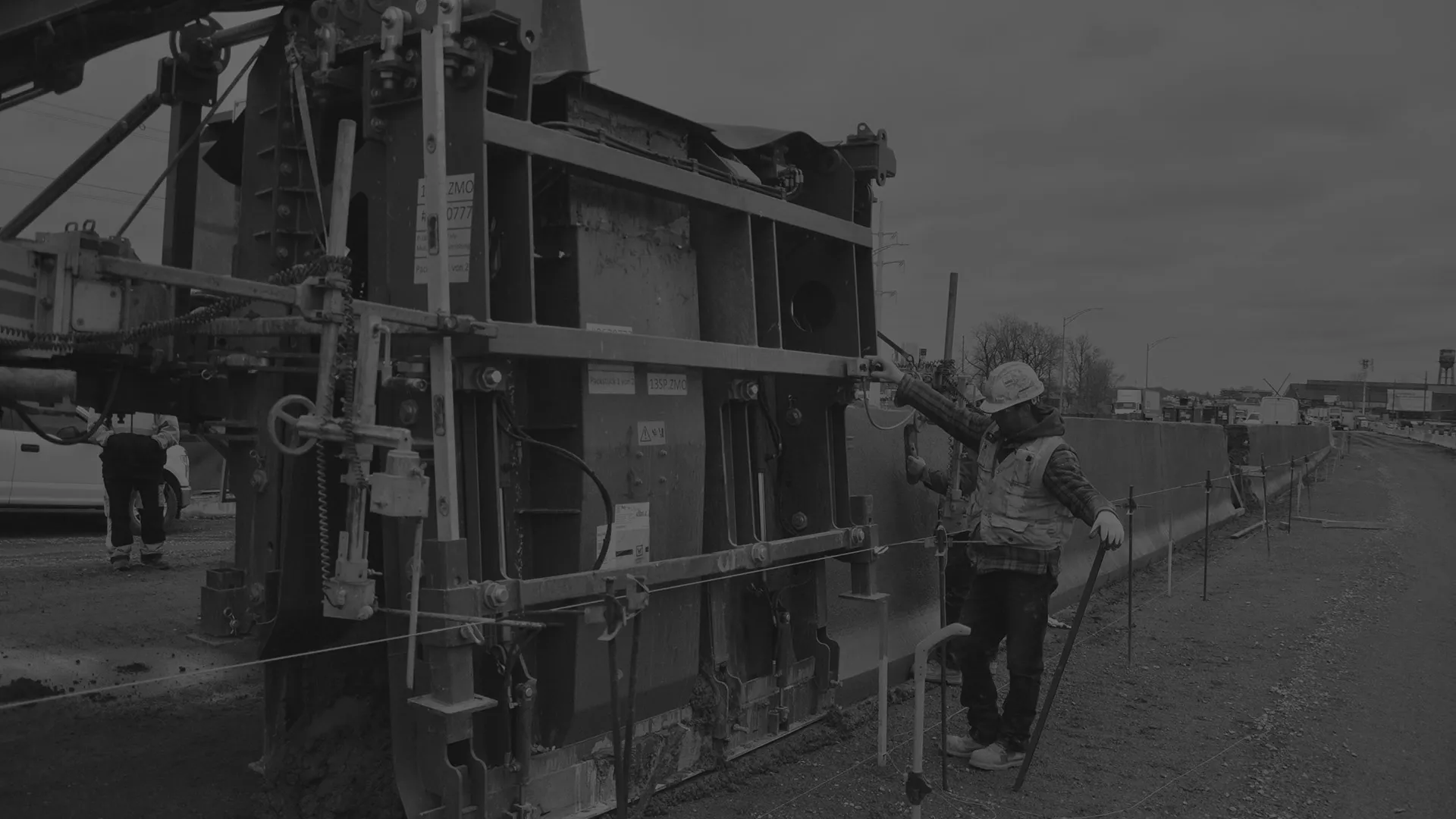 Travailleur de la construction avec casque et gilet de sécurité manipule un grand équipement de coffrage sur un chantier routier.