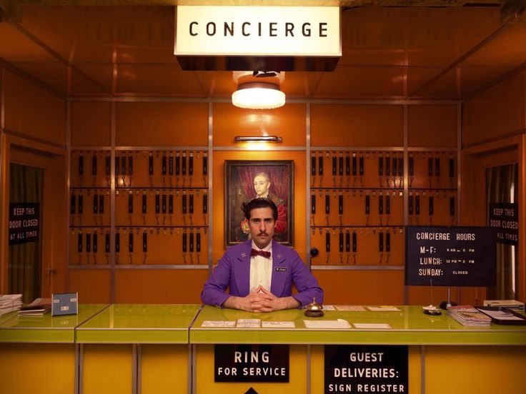 This may contain: a man in a purple shirt and bow tie sitting at a counter with signs on it