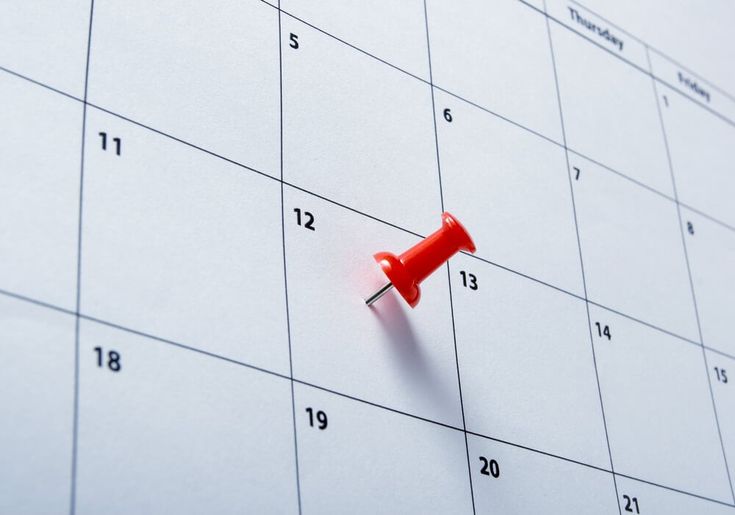 This may contain: a red push pin sitting on top of a calendar