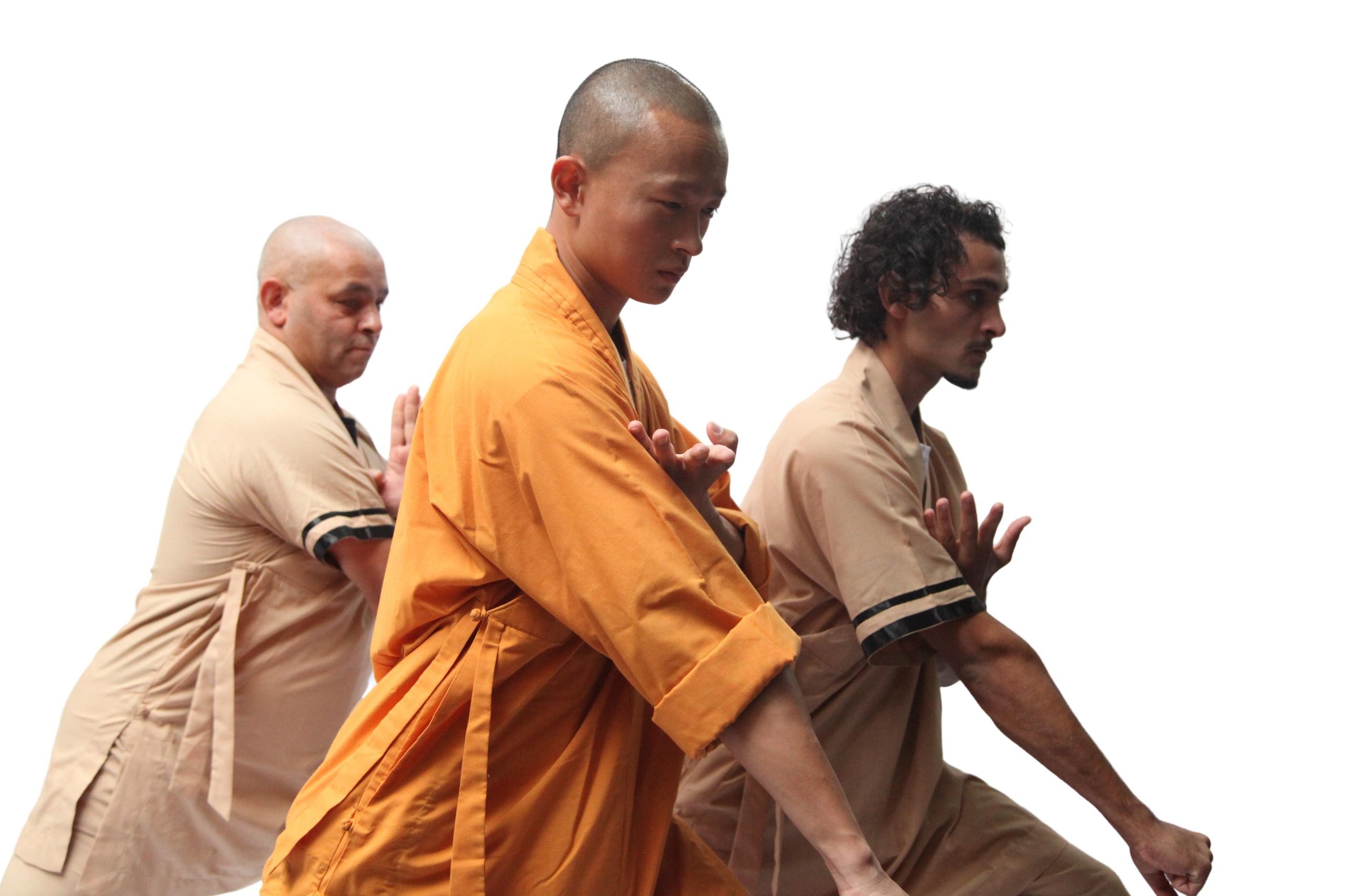 Three Asian men practicing martial arts in focused poses, wearing traditional robes with one in orange and two in beige.