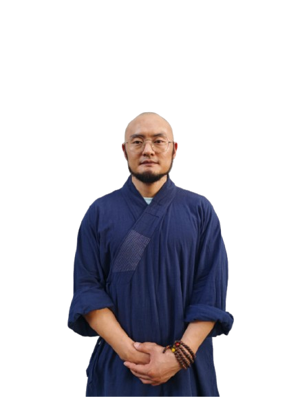 Bald man with glasses wearing a blue traditional robe and wooden bead bracelets, standing with hands clasped.