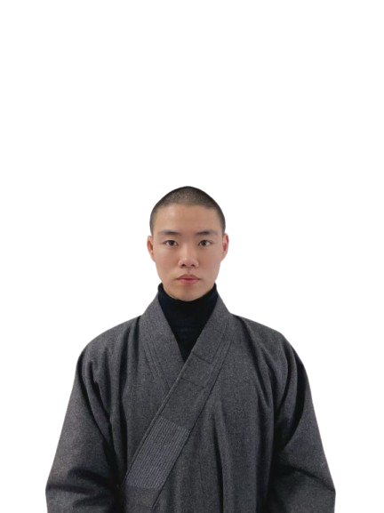 Man with a shaved head wearing a dark gray traditional robe and black turtleneck.
