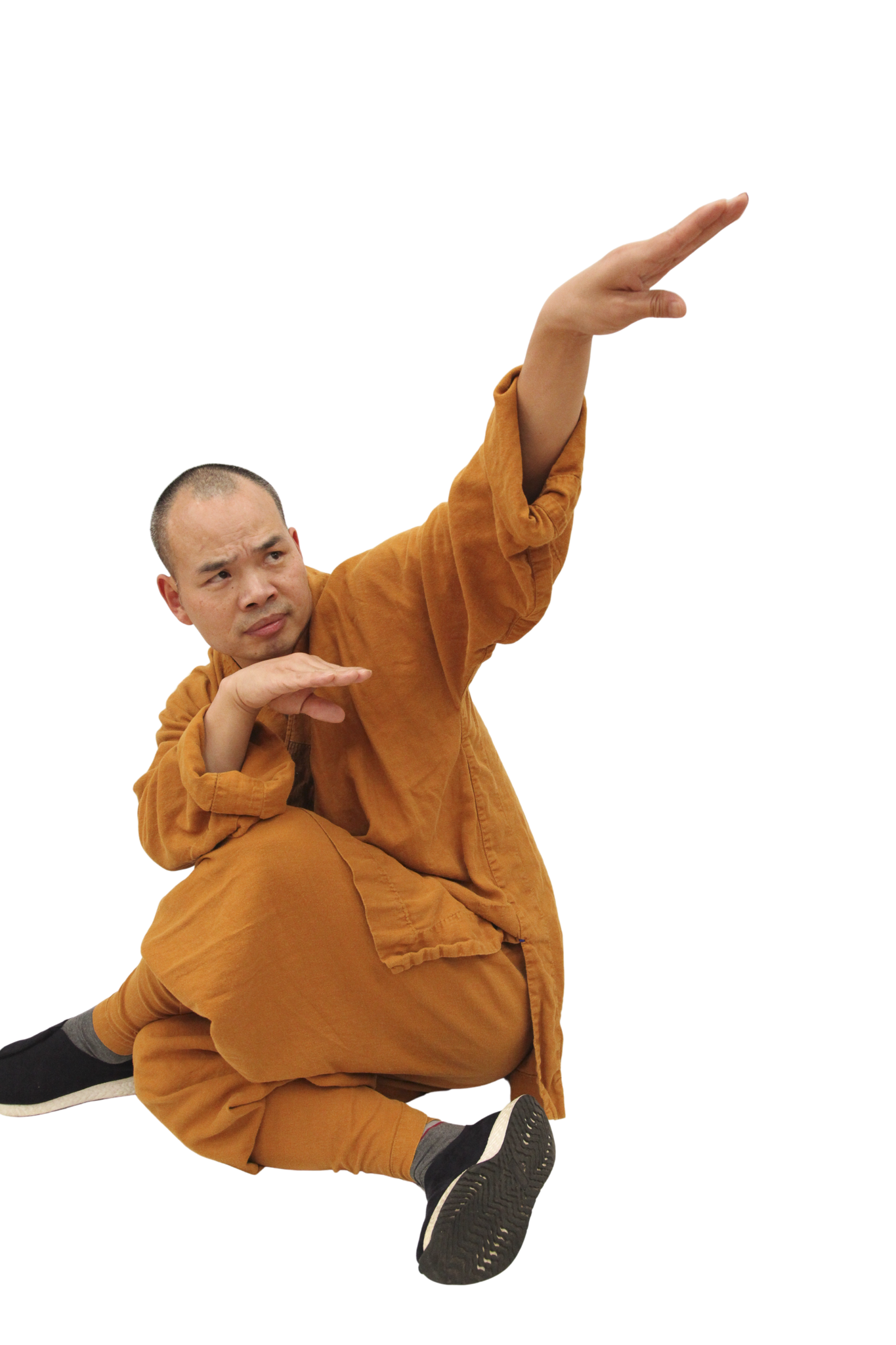 A man dressed in orange traditional clothing performing a martial arts pose with one leg bent and arms extended.martial art london Shaolin Xiu