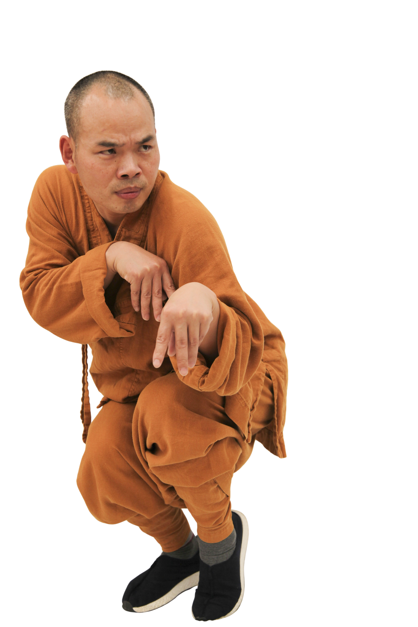 A man in orange traditional monk clothing squats with hands positioned in a martial arts stance, looking focused.