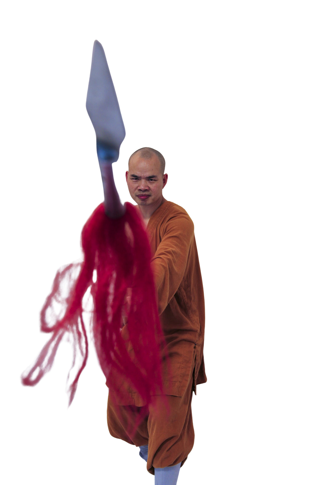 Martial artist in orange traditional attire holding a spear with red tassel in a forward stance.