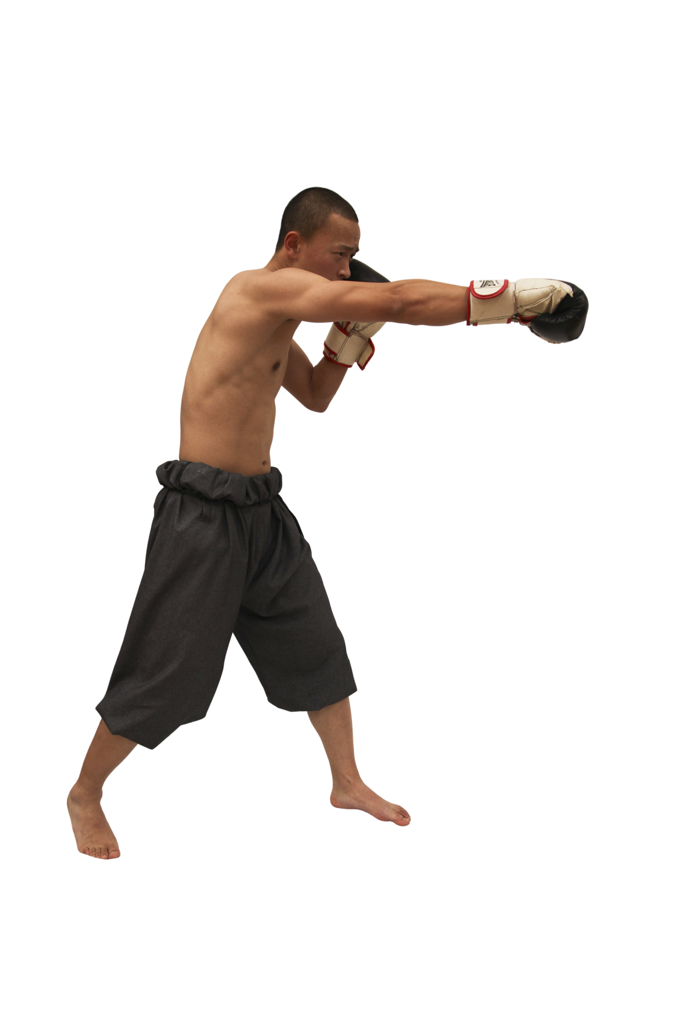 Shirtless male martial artist in gray hakama pants throwing a punch while wearing boxing gloves.
