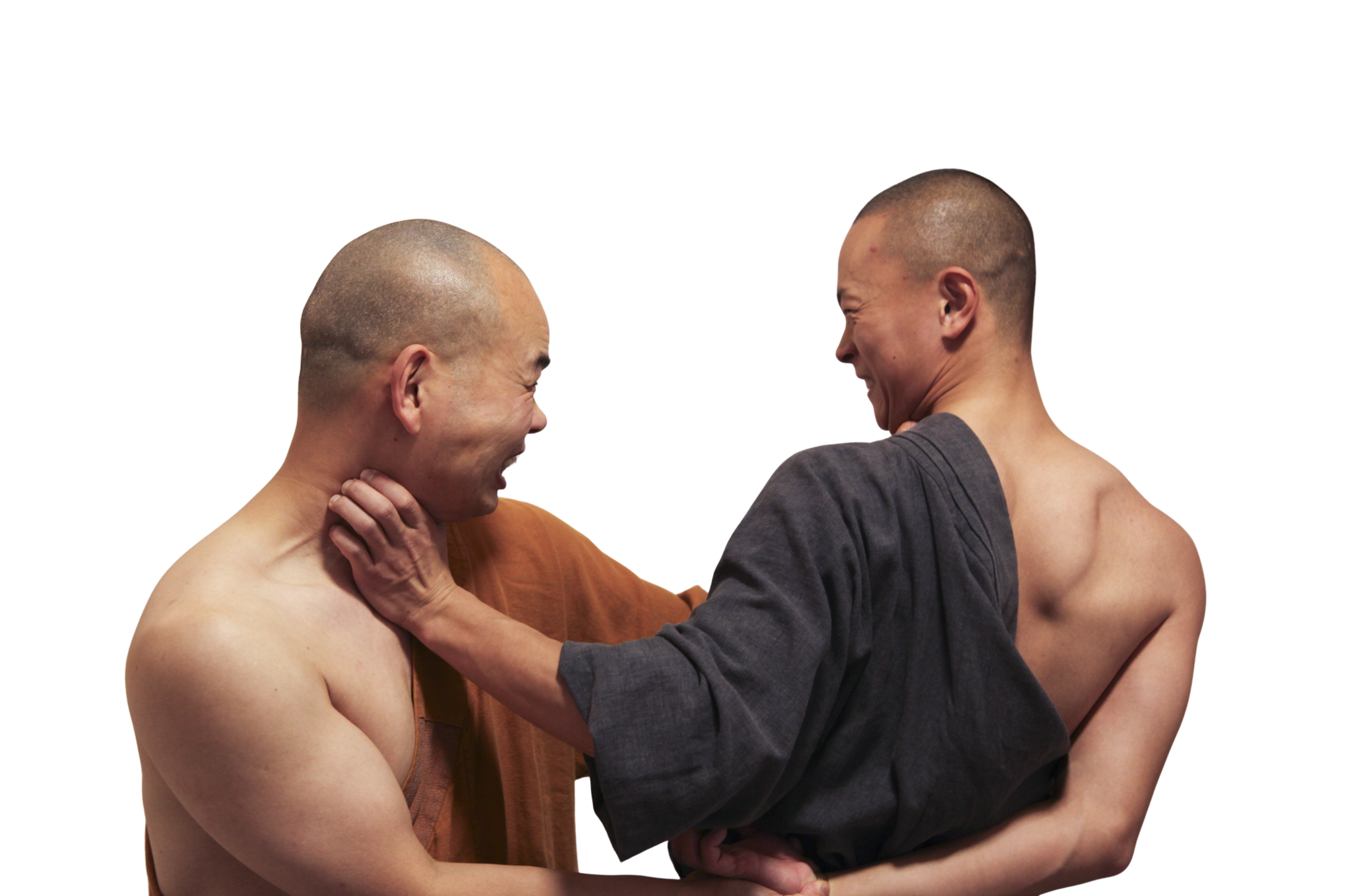 Two shirtless men with shaved heads facing each other, one wearing a brown robe and the other a gray robe, smiling and engaging in a friendly interaction.martial art london Shaolin Xiu