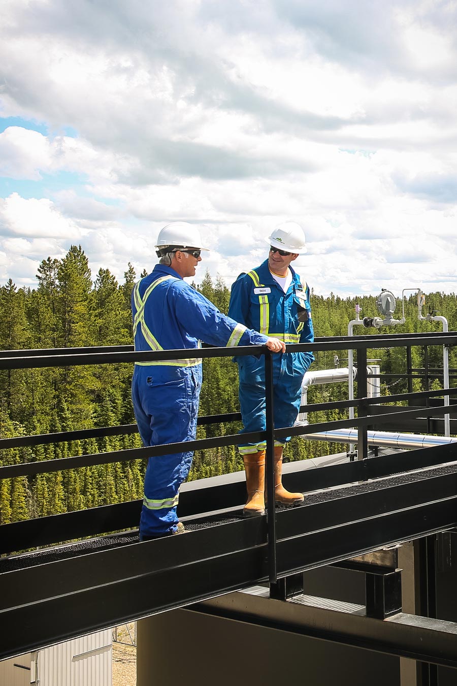Two operators standing on a metal walkway overlooking a pump jack