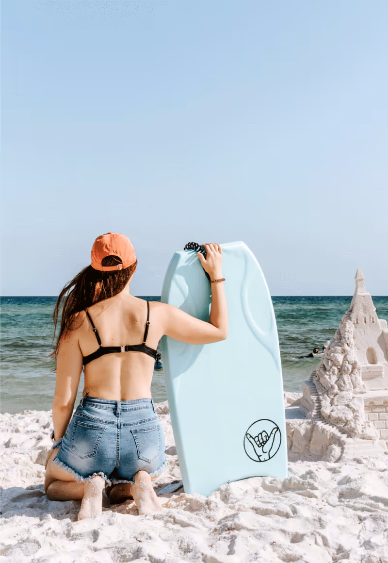 Girl holding body board next to a sand castle