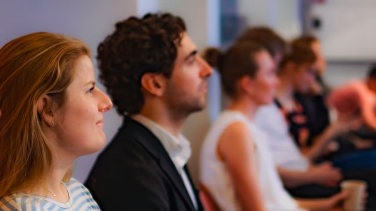 Side view of a group of people sitting in a row, attentively looking forward.