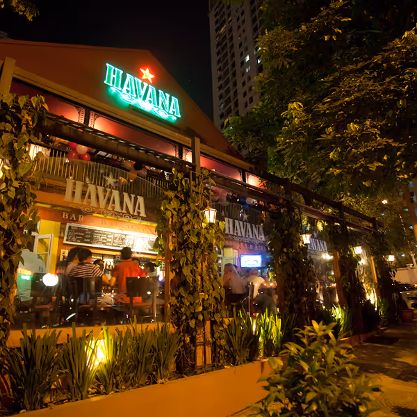Night view of Havana Bar with people inside, illuminated signage, and surrounding greenery.